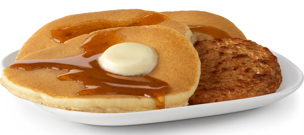 A stack of buttered pancakes with syrup and sausage links, served at the brunch